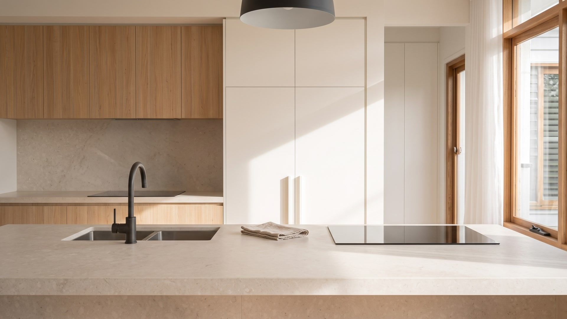 The same kitchen after a clean: a clear bench, a folded tea towel and a shining cooktop